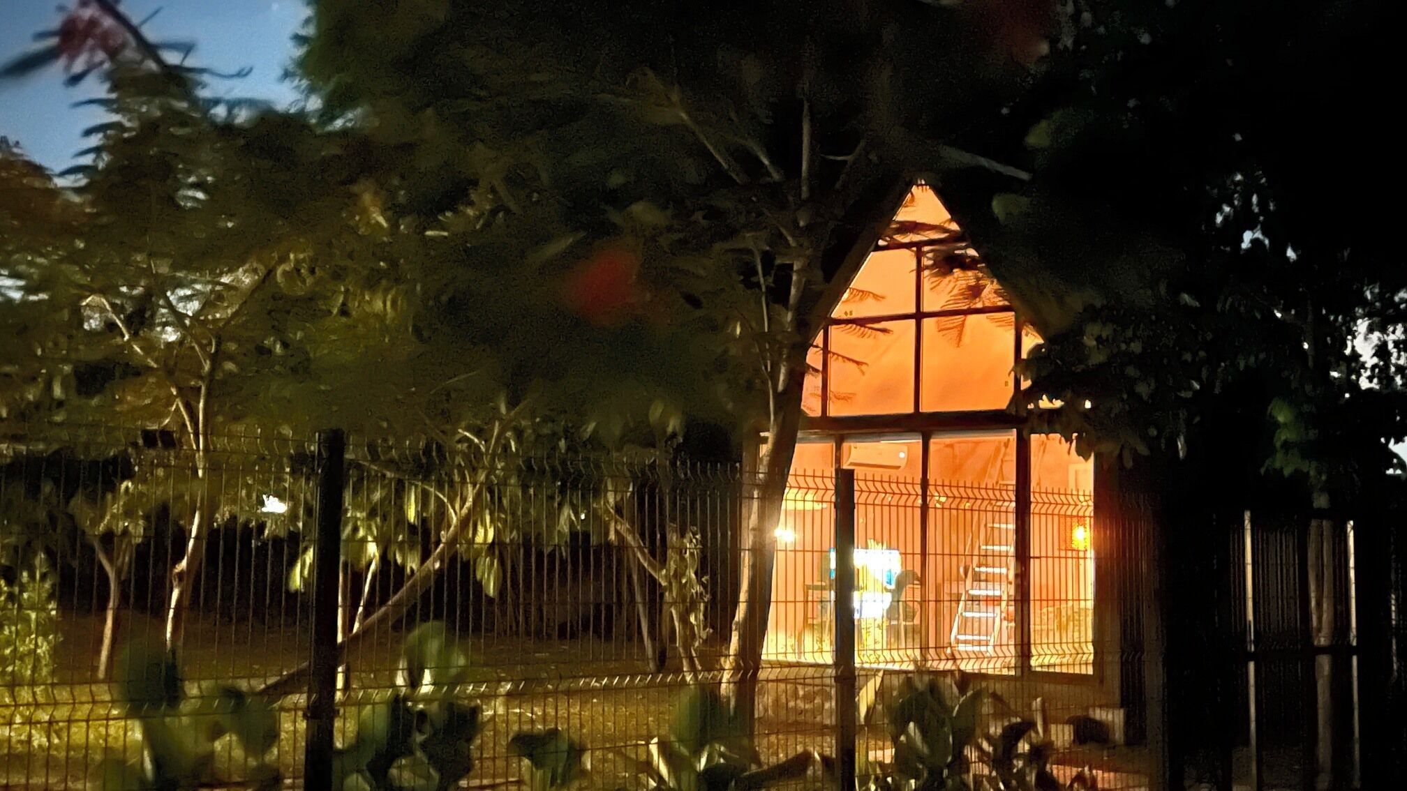 A cozy, enclosed structure with a warm interior, surrounded by a metal fence and trees.