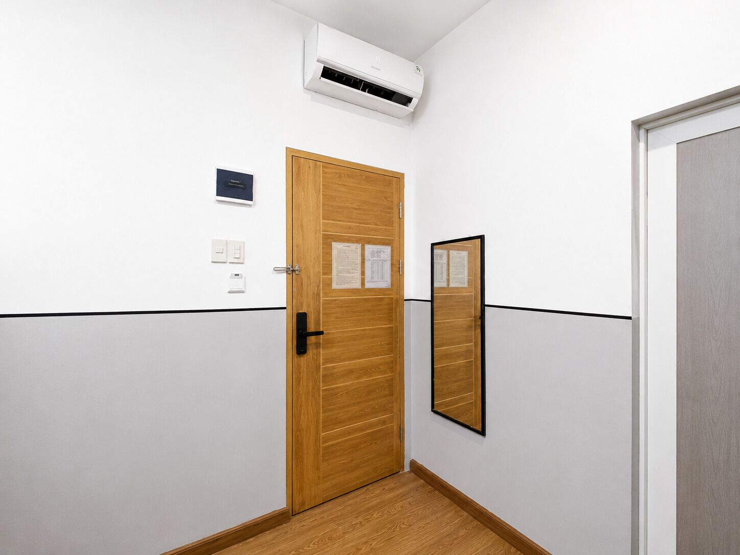 A hallway with a wooden door, a wall-mounted air conditioning unit, and a door mirror.