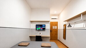 Una habitación de hotel con cama, escritorio con monitor de computadora, puerta de madera y aire acondicionado instalado en la pared.