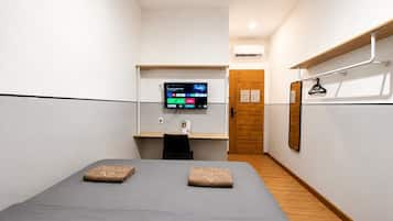 Une chambre d’hôtel avec un lit, un bureau doté d’un écran d’ordinateur, une porte en bois et un climatiseur fixé au mur.