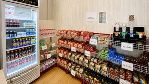 Un dispensador de bebidas refrigeradas y estantes llenos de aperitivos y condimentos.