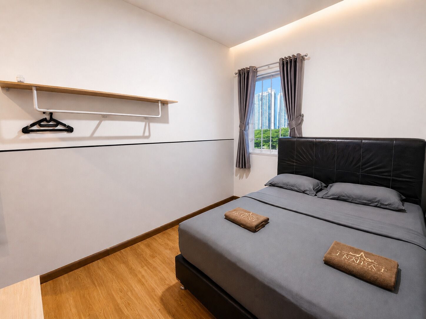A bedroom with a bed, a window with curtains, a wooden floor, and a wall-mounted shelf.