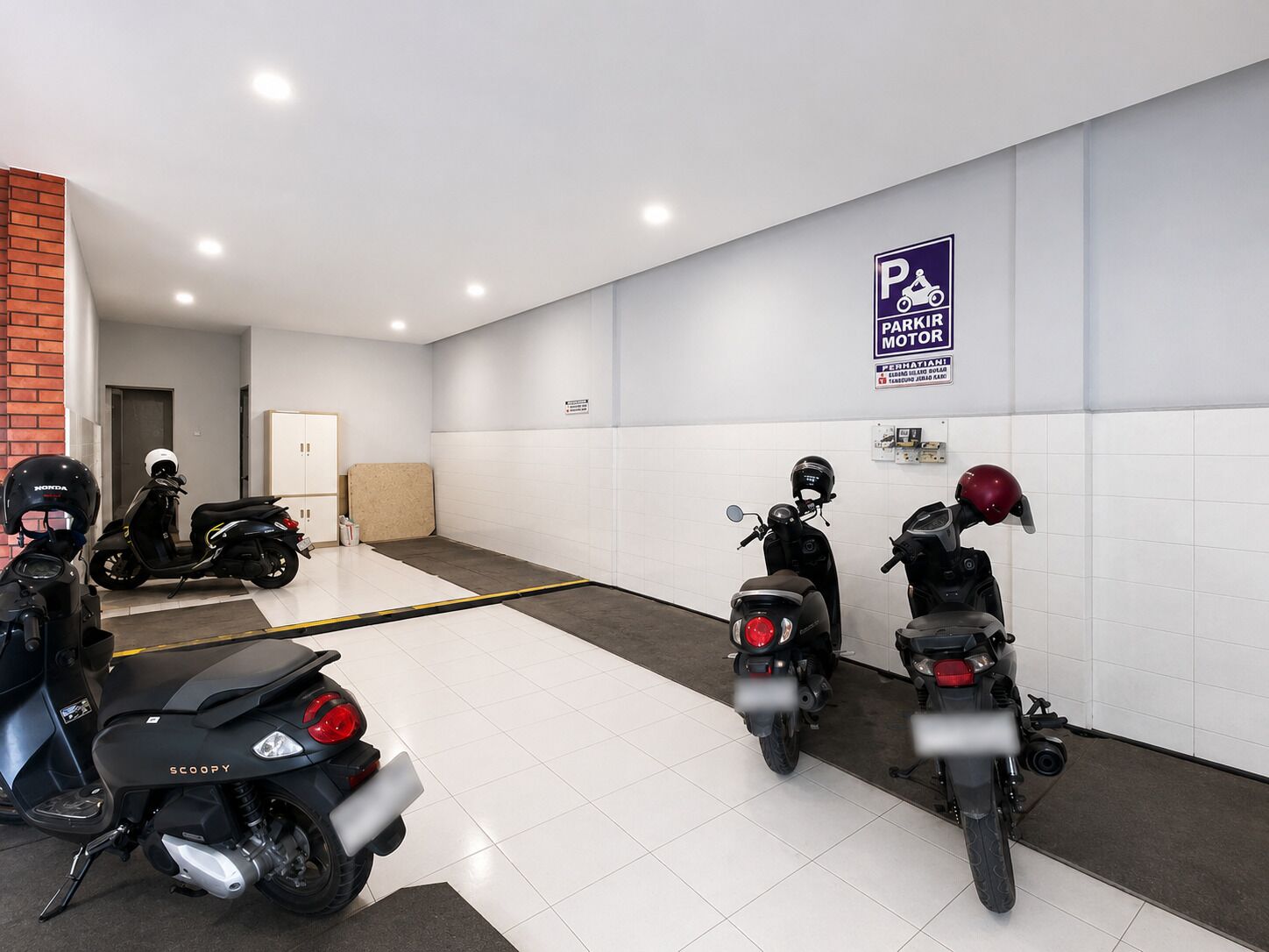 Een parkeerplaats met scooters en motorfietsen, een bord met daarop aanduiding voor motorvoertuigen en een deur die naar een ruimte leidt.