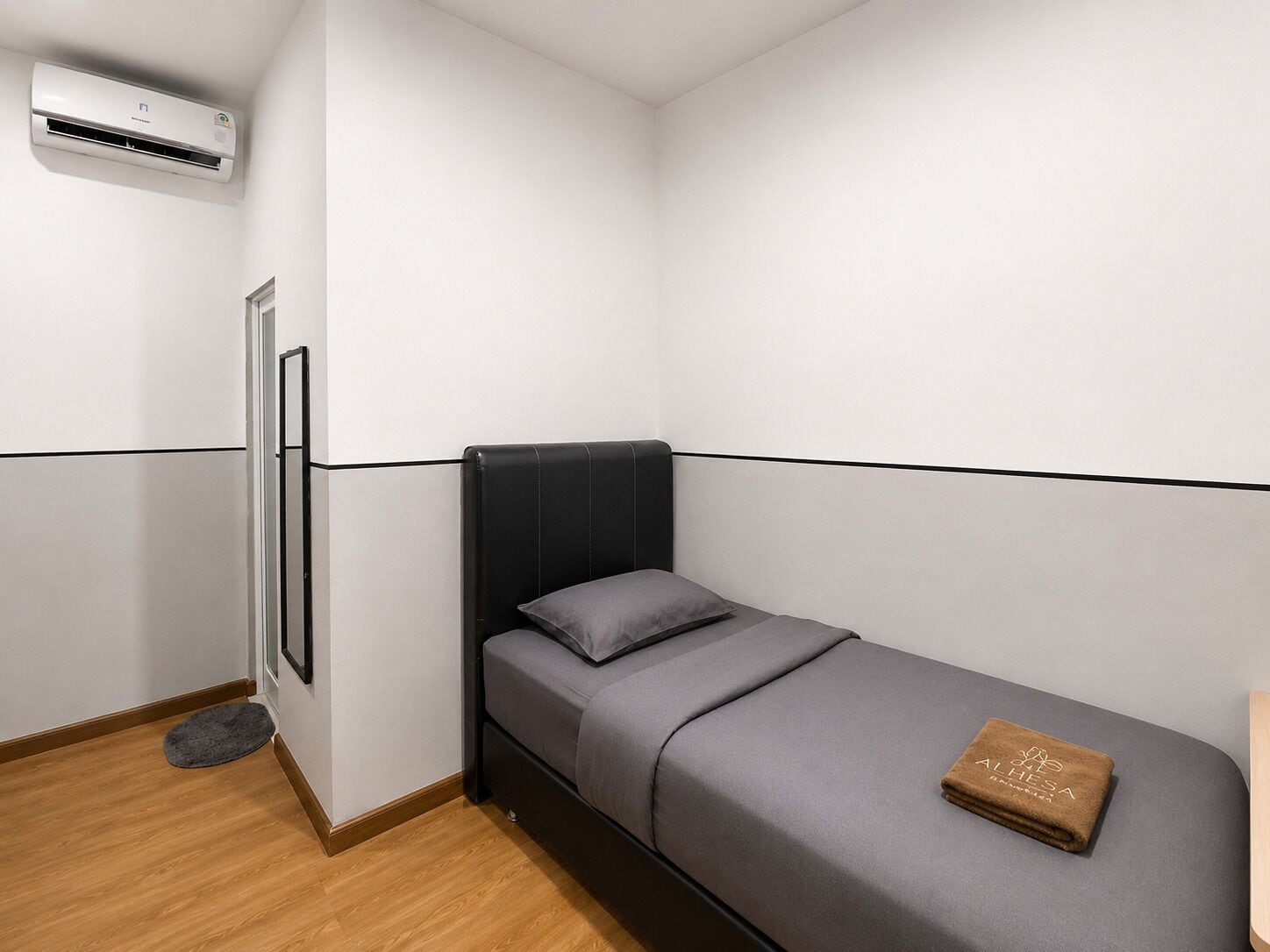 A small, modern bedroom with a single bed, a bedside table, and a wall-mounted air conditioning unit.