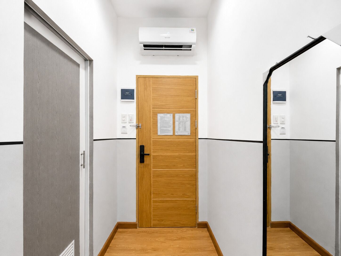 A hallway with a wooden door, an air conditioning unit above, and a black security camera on the right wall.