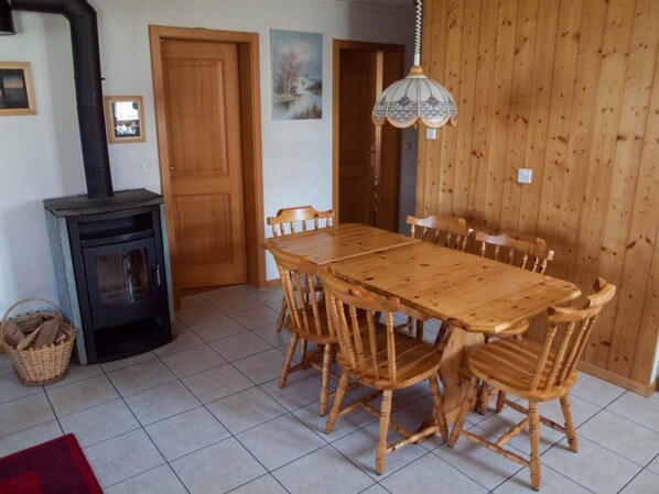 A dining area with a wooden table and chairs, a black stove, and a wooden wall.