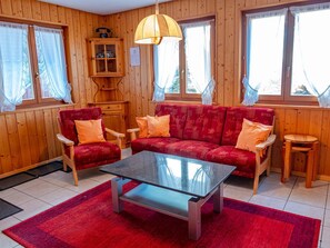 Um quarto aconchegante com paredes de madeira, um sofá vermelho, uma mesa de centro de vidro e um armário de madeira com um telefone.