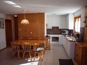 Cozinha compacta com armários de madeira, mesa de jantar com cadeiras, micro-ondas e pia.