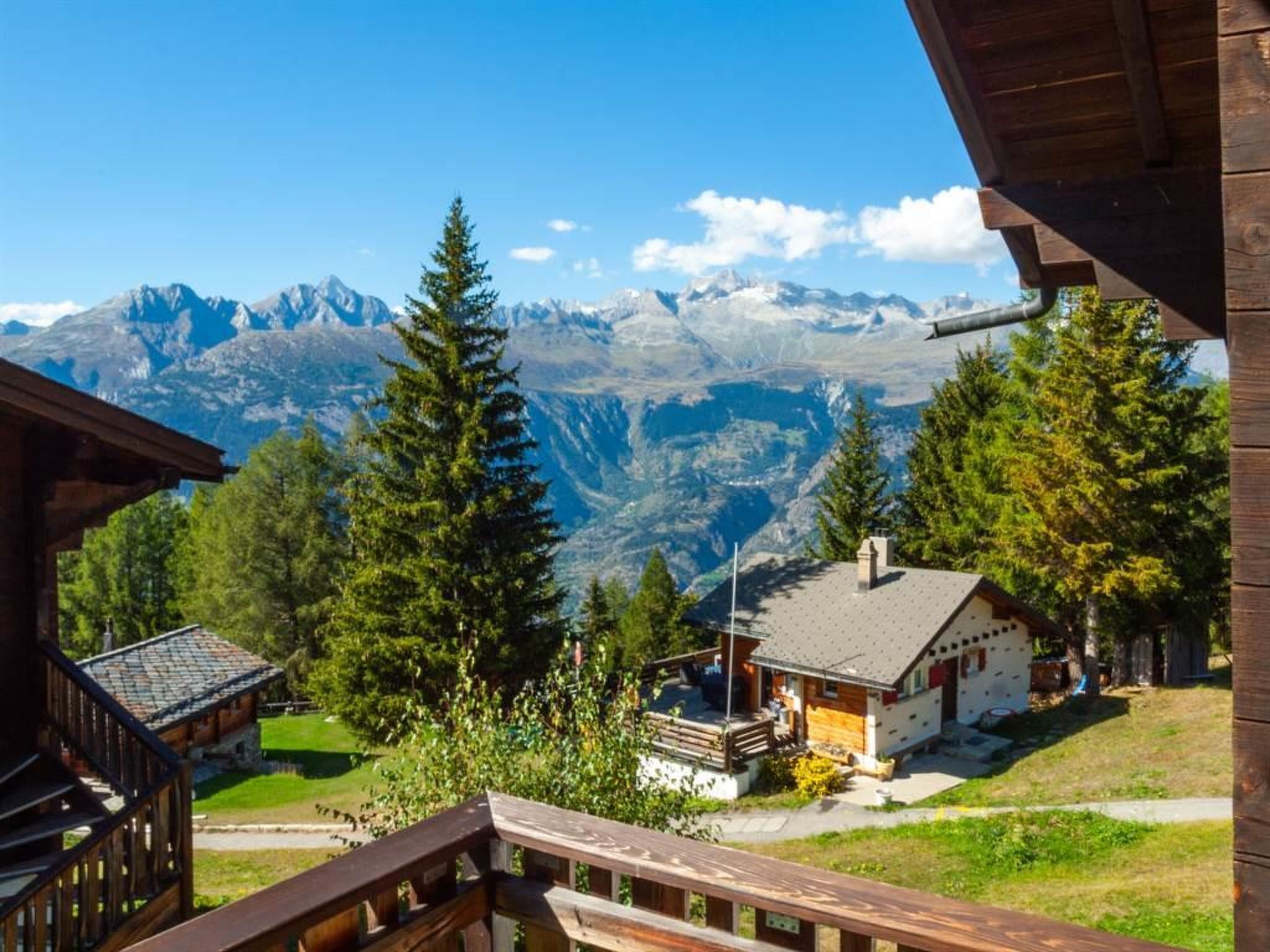A mountain lodge with a wooden deck, a small cabin, and a view of snow-capped peaks.