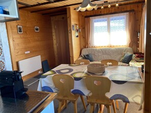 A cozy cabin interior with a dining table, chairs, a sofa, and a window with curtains. - Chalet Bambi Appartement/Fewo, Dusche, WC 4-Bettwohnung by Interhome (Rosswald)