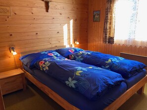 A wooden cabin bedroom with a bed, two bedside lamps, and a wooden headboard. - Chalet Bambi Appartement/Fewo, Dusche, WC 4-Bettwohnung by Interhome (Rosswald)