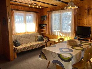 A cozy cabin interior with a sofa, a dining table, and a television. - Chalet Bambi Appartement/Fewo, Dusche, WC 4-Bettwohnung by Interhome (Rosswald)