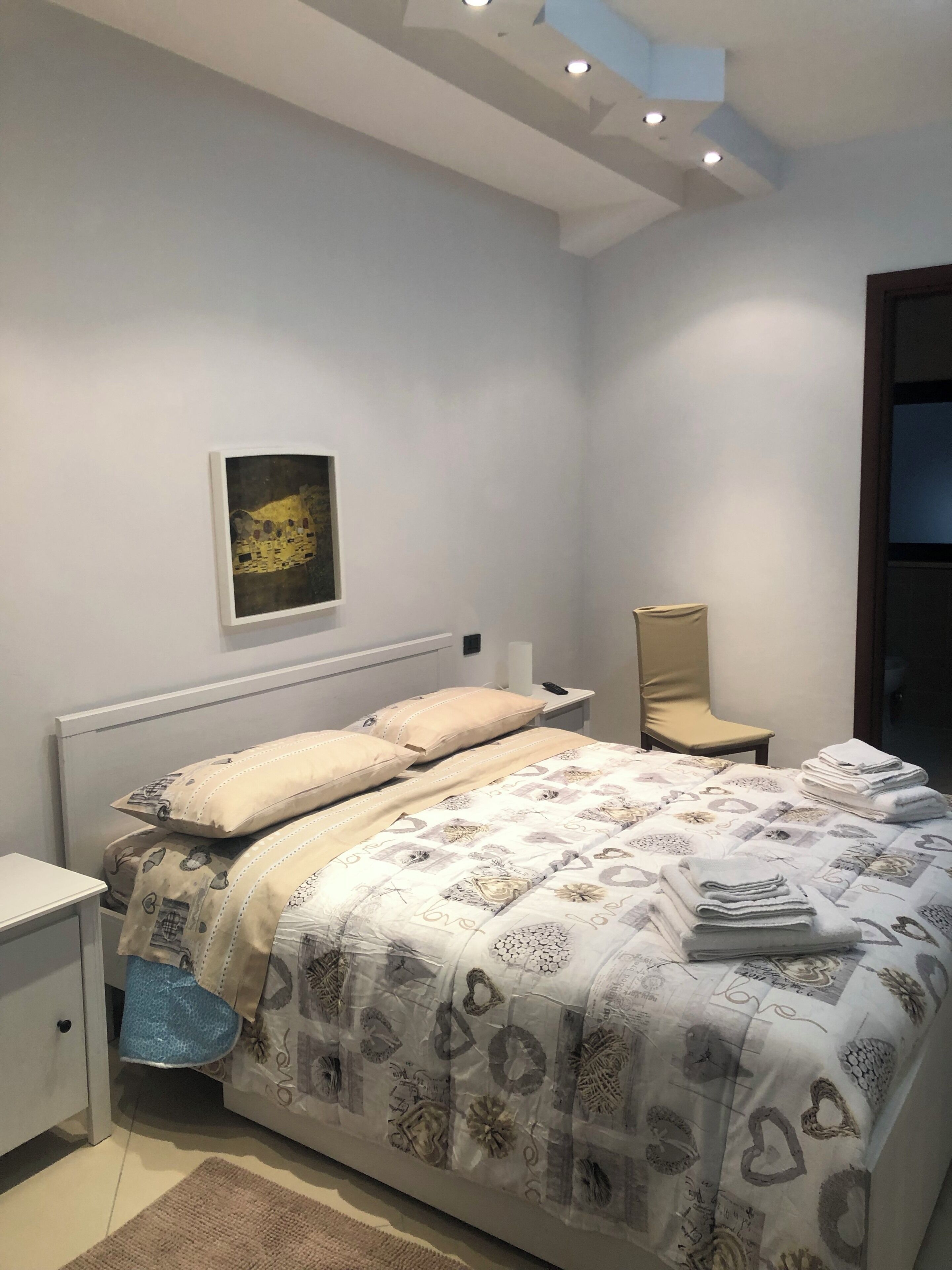 Un dormitorio con cama, una silla, un escritorio y un cuadro en la pared.