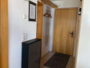 Ein Flur mit einer Holztür, einem schwarzen Schrank, einem gerahmten Aushang und einem Kleiderhaken mit Kleiderbügeln.