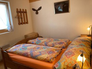 Ein Bett mit farbenfroher Bettwäsche, ein hölzerner Kopfteil, ein Wandmantelhalter, eine Elchdekoration und ein gerahmtes Schmetterlingsbild.