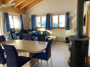 Ein Zimmer mit Esstisch, Stühlen, einer Couch, einem Kamin und Fenstern mit Vorhängen.