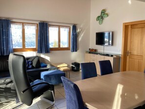 A modern living room with a sofa, a dining table, chairs, a TV, and a view of the outdoors. - Chalet Lalula Appartement/Fewo, Dusche, WC Appartement/Fewo, Dusche, WC by Interhome (Rosswald)