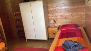 Quarto com cama, guarda-roupa, mesinha com abajur e tapete vermelho.