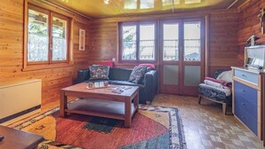 Interior acolhedor de uma cabana com decoração em madeira, um sofá, uma mesa de centro e uma pequena cozinha.