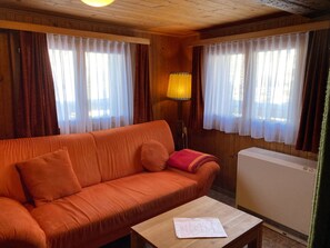 A room with a wooden ceiling, a sofa, a table with a document, and a radiator. - Chalet Alphütte Appartement/Fewo, Dusche, WC 4-Bettwohnung Erdgeschoss by Interhome (Rosswald)