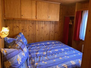 Et soveværelse med et træskab, en seng med et blomstret blåt sengetæppe og en lampe til venstre.