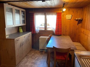 A compact kitchen with wooden cabinets, a small refrigerator, and a dining table with chairs. - Chalet Alphütte Appartement/Fewo, Dusche, WC 4-Bettwohnung Erdgeschoss by Interhome (Rosswald)
