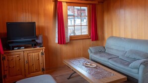 Un interior de madera con un televisor sobre un mueble bajo, un sofá y una mesa con un diseño decorativo.