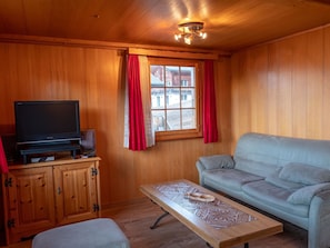 Ein Holzinterieur mit einem Fernseher auf einer Kommode, einem Sofa und einem Tisch mit dekorativer Musterung.
