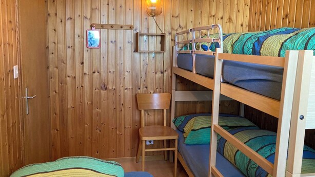 Ein Zimmer mit einem Holzbett mit Etagen, einem Schreibtisch, einem Stuhl, einer Wandlampe und einem Fenster.