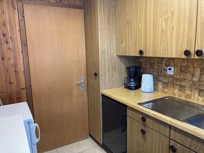 Eine kleine Küche mit Holzschränken, einer Kaffeemaschine und einem Spülbecken.