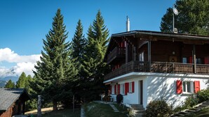 Ein Chalet mit Balkon, umgeben von Bäumen und einem Berg im Hintergrund.
