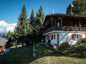 Ein Chalet mit Balkon, umgeben von Bäumen und einem Berg im Hintergrund.