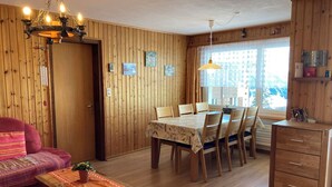 Ein gemütliches Zimmer mit Esstisch, Stühlen, einer Couch, einem Holzschrank und einer Pendelleuchte.