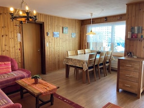 Ein gemütliches Zimmer mit Esstisch, Stühlen, einer Couch, einem Holzschrank und einer Pendelleuchte.
