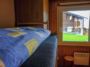 A bedroom with a bed, a window, a wooden wall, and a small stool. - Fletschhorn EG 4-Bettwohnung, Dusche, WC 4-Bettwohnung by Interhome (Rosswald)
