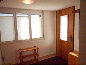 A room with a wooden door, a small wooden bench, and three windows with blinds. - Fletschhorn EG 4-Bettwohnung, Dusche, WC 4-Bettwohnung by Interhome (Rosswald)