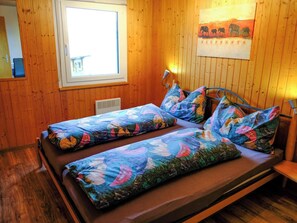A wooden room with a bed featuring floral bedding and a wall-mounted lamp. - Fletschhorn EG 4-Bettwohnung, Dusche, WC 4-Bettwohnung by Interhome (Rosswald)