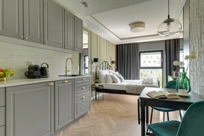 A modern hotel room with a kitchenette, a bed with white bedding, a dining area with a table and chairs, and a view of the outside. - Rezydencja Wintera 1B | River View (Gdańsk)