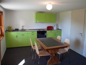 Een kleine keuken met groene kastjes, een eettafel en stoelen.