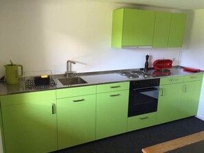 A kitchen with green cabinets, a sink, a stove, and a red appliance. - Chalet Bergfink 4-Bettwohnung, Dusche, WC 4-Bettwohnung by Interhome (Rosswald)