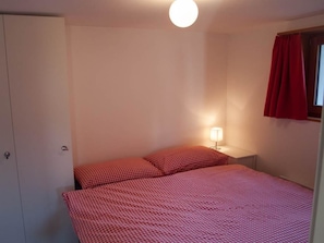 A bedroom with a bed, a nightstand, a lamp, a wardrobe, and a window with curtains. - Chalet Bergfink 4-Bettwohnung, Dusche, WC 4-Bettwohnung by Interhome (Rosswald)