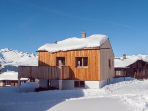 Een houten chalet met een balkon, omringd door met sneeuw bedekte bergen.
