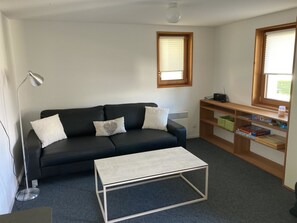 Een moderne woonkamer met een zwarte bank, een witte salontafel, een vloerlamp en een houten boekenkast.