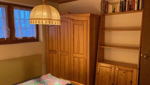 A bedroom with a bed, a wooden wardrobe, a shelf with books, and a window with curtains. - Chalet Gerbera Appartement/Fewo, Bad, WC 5-Bettwohnung by Interhome (Rosswald)