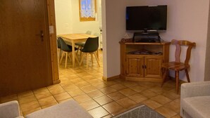 A room with a wooden door, a dining table with chairs, a television on a stand, and a cabinet. - Chalet Gerbera Appartement/Fewo, Bad, WC 5-Bettwohnung by Interhome (Rosswald)