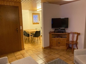 A room with a wooden door, a dining table with chairs, a television on a stand, and a cabinet. - Chalet Gerbera Appartement/Fewo, Bad, WC 5-Bettwohnung by Interhome (Rosswald)