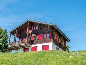 Un chalet de madera de dos pisos con contraventanas rojas, un balcón y una antena parabólica.