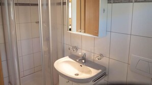 Ein Badezimmer mit Duschkabine aus Glas, einem Waschbecken mit Spiegel darüber und gefliesten Wänden.