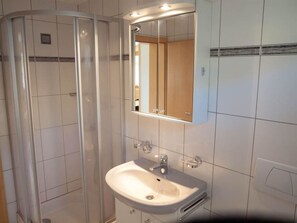 Ein Badezimmer mit Duschkabine aus Glas, einem Waschbecken mit Spiegel darüber und gefliesten Wänden.