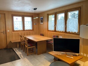 A room with a wooden dining table, chairs, a TV, and windows with curtains. - Chalet Fridi 4-Bettwohnung, Dusche, WC 4-Bettwohnung Erdgeschoss by Interhome (Rosswald)